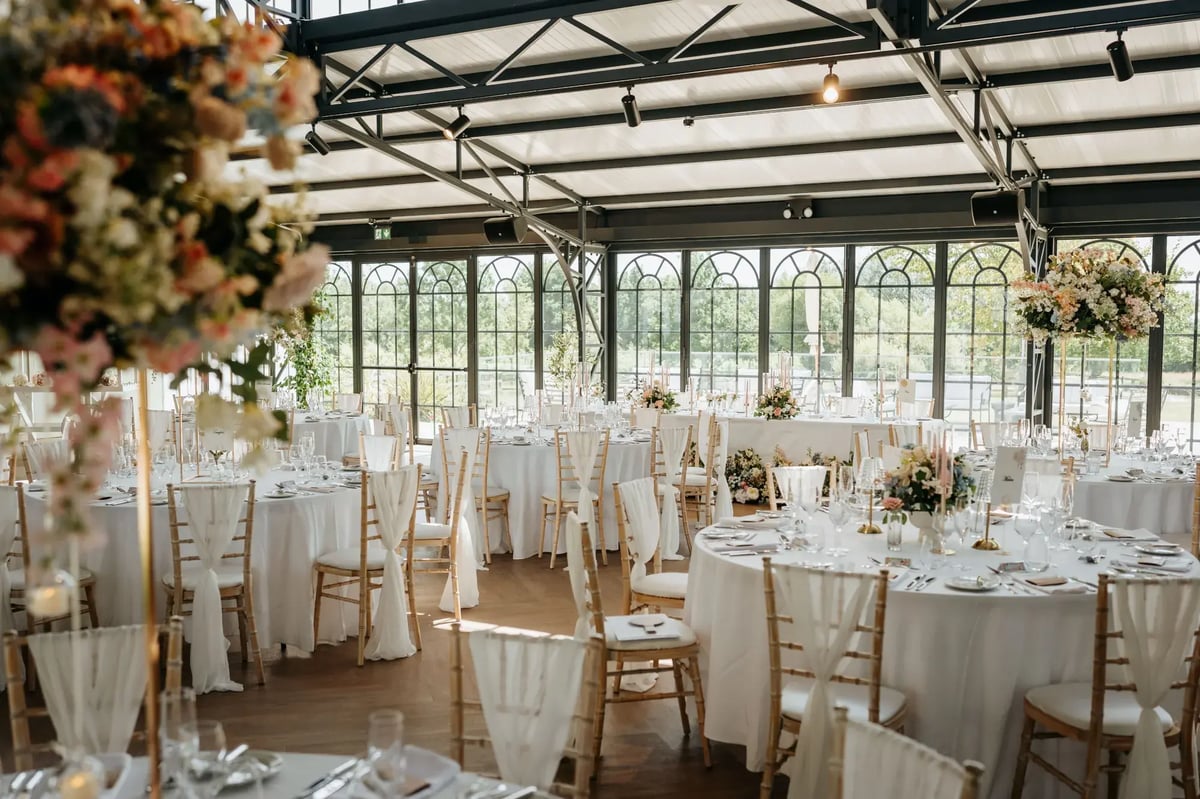 Circle tables dressed for a wedding with colourful flowers in the Orangery at High House
