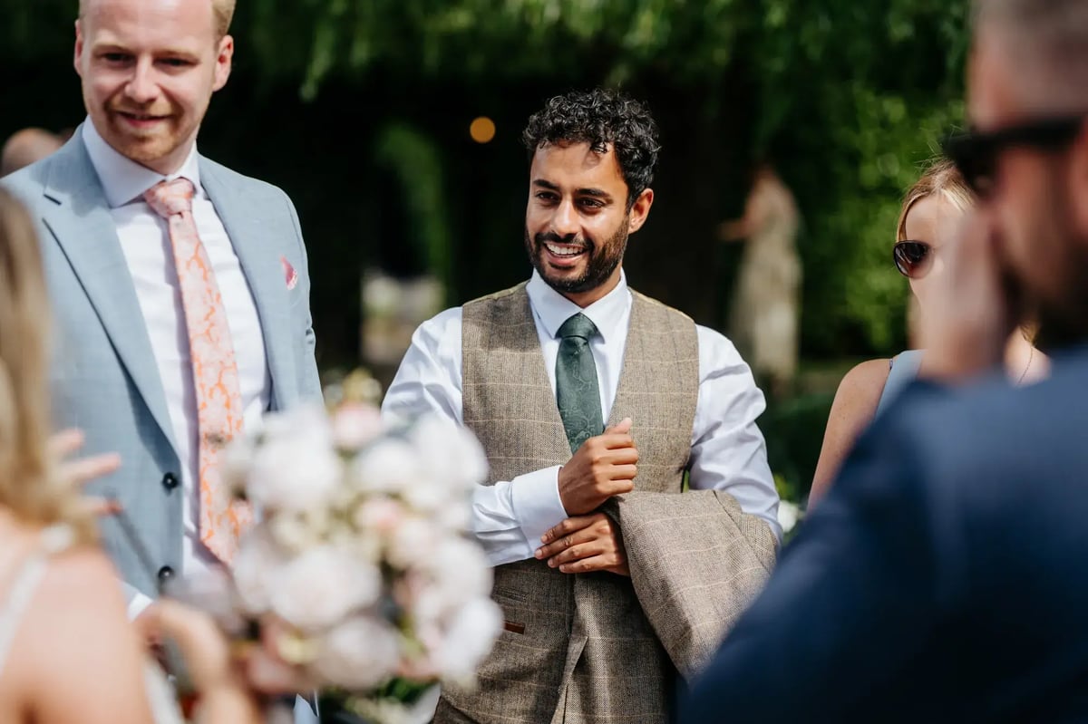 Wedding guest holding blazer talking outside at High House