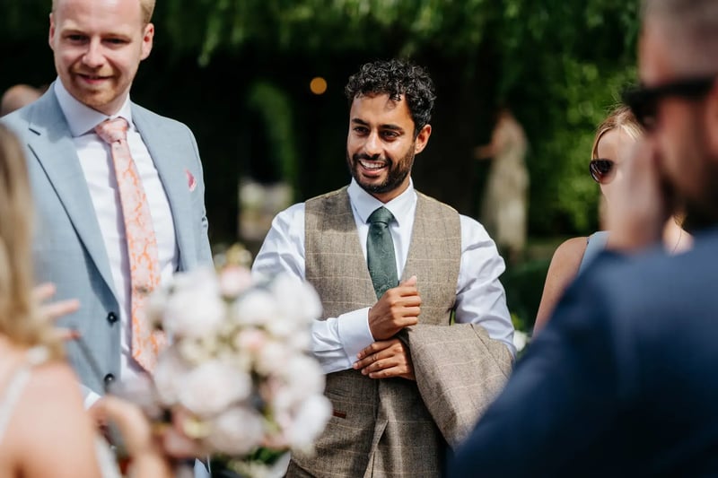 Wedding guest holding blazer talking outside at High House
