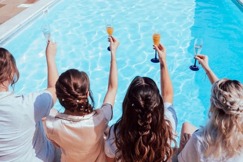 Bride and bridesmaids holding a drink by the pool outside the dressing room at High House